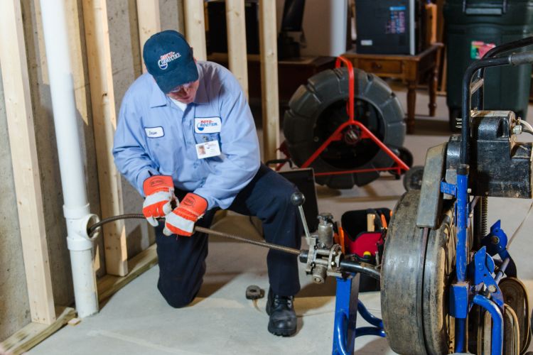 Experienced plumber using a Roto Rooter tool to clean a plastic pipe