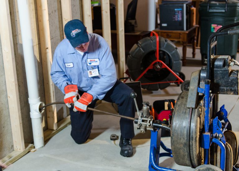 Experienced plumber using a Roto Rooter tool to clean a plastic pipe