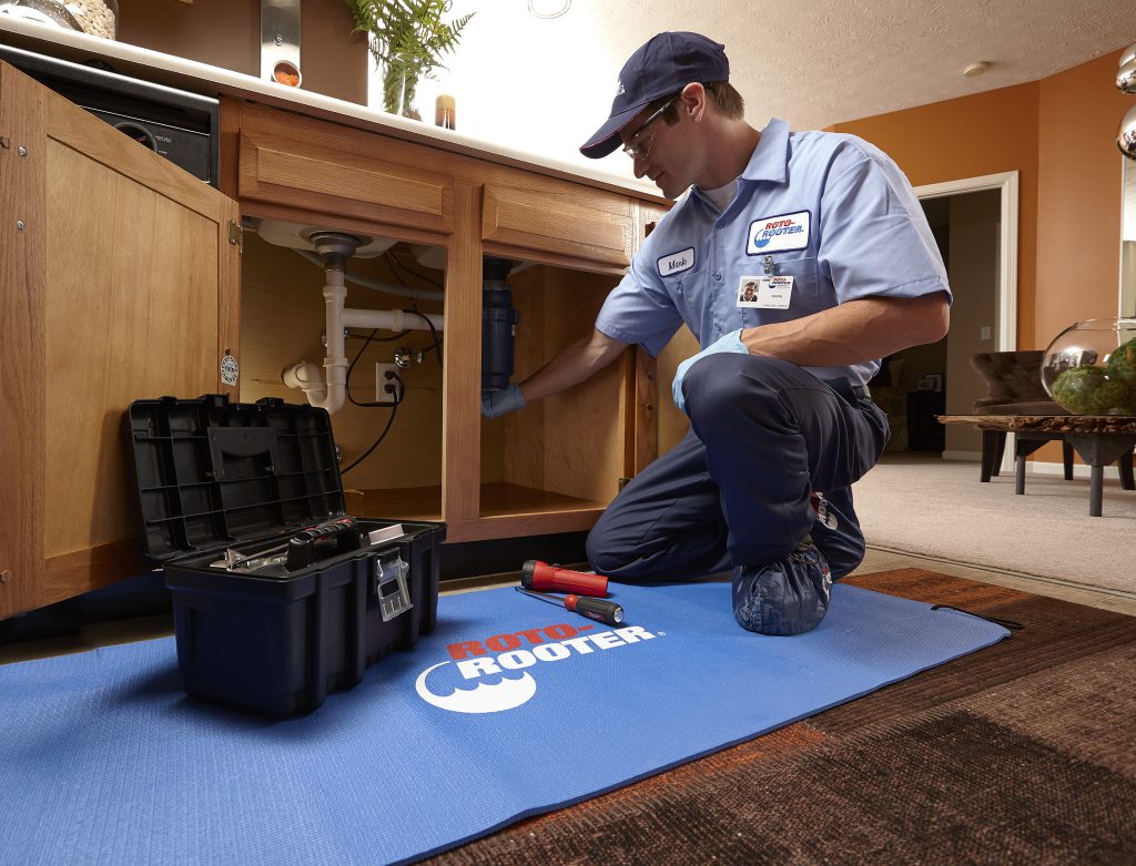 RotoRooter plumber performing a drain repair on a kitchen sink